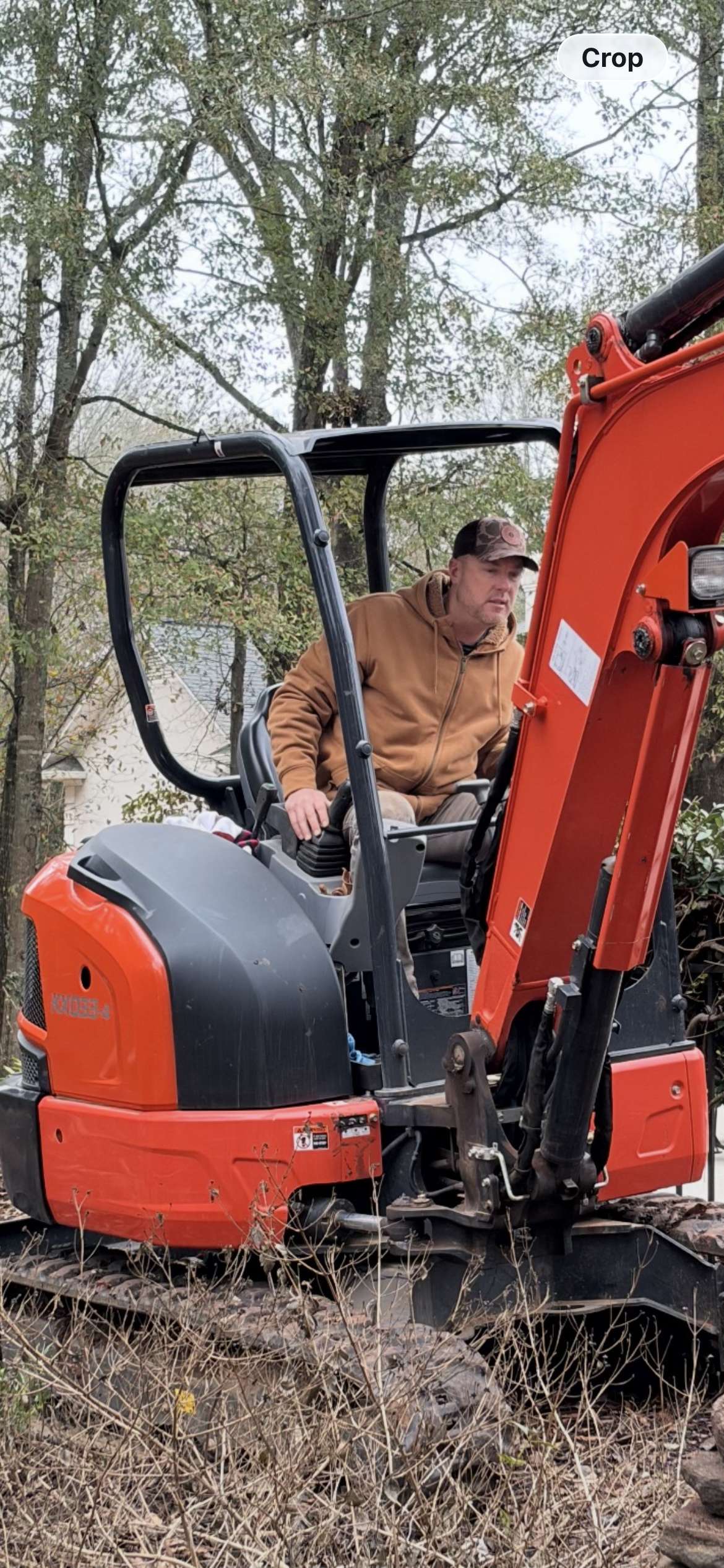 Jamie Bannister operating an orange excavator on a wooded landscaping project