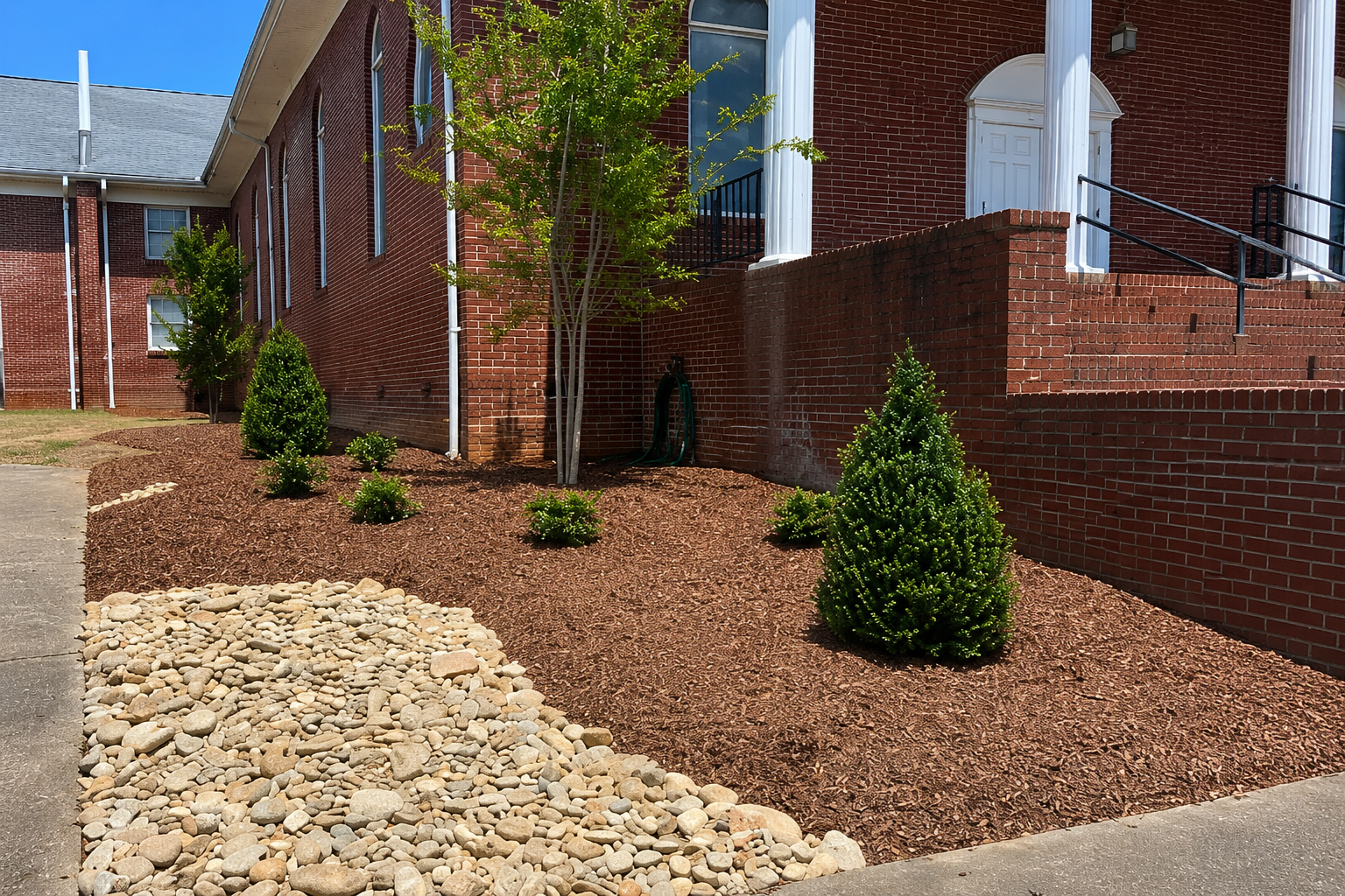 Completed river-rock drainage feature with compact landscaping equipment in a wooded yard